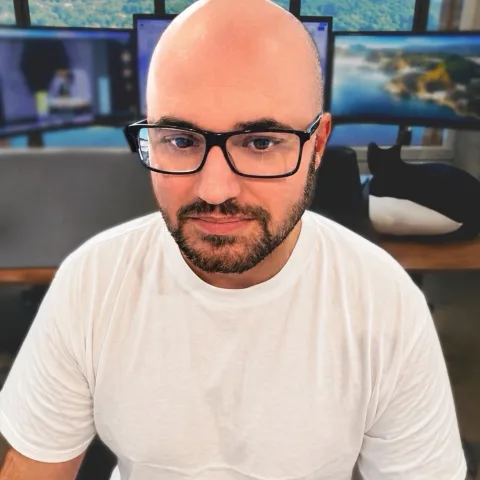 Greg McGuirk, smiling at his desk in front of three monitors